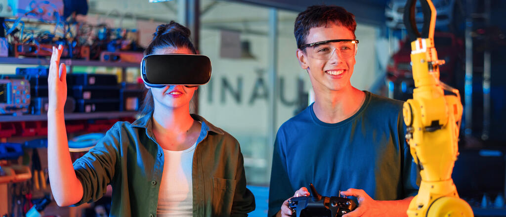 Eine Schülerin mit VR-Brille, ein Schüler steuert einen Roboter